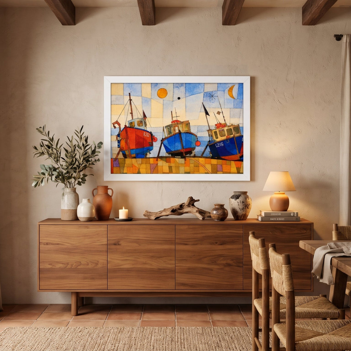 A framed colorful painting of three boats on a beach hangs on a beige wall in a rustic dining room with a wooden sideboard, table, chairs, and large windows.