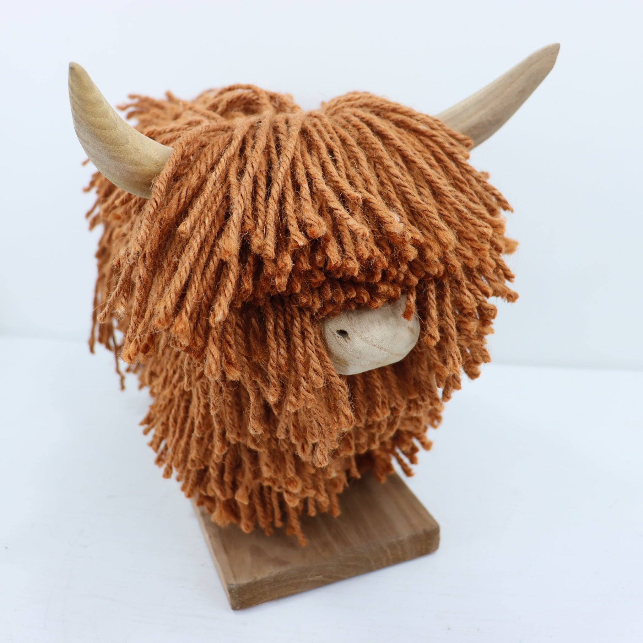 Yarn-braided sculpture of a highland cow head on a wooden base against a white background