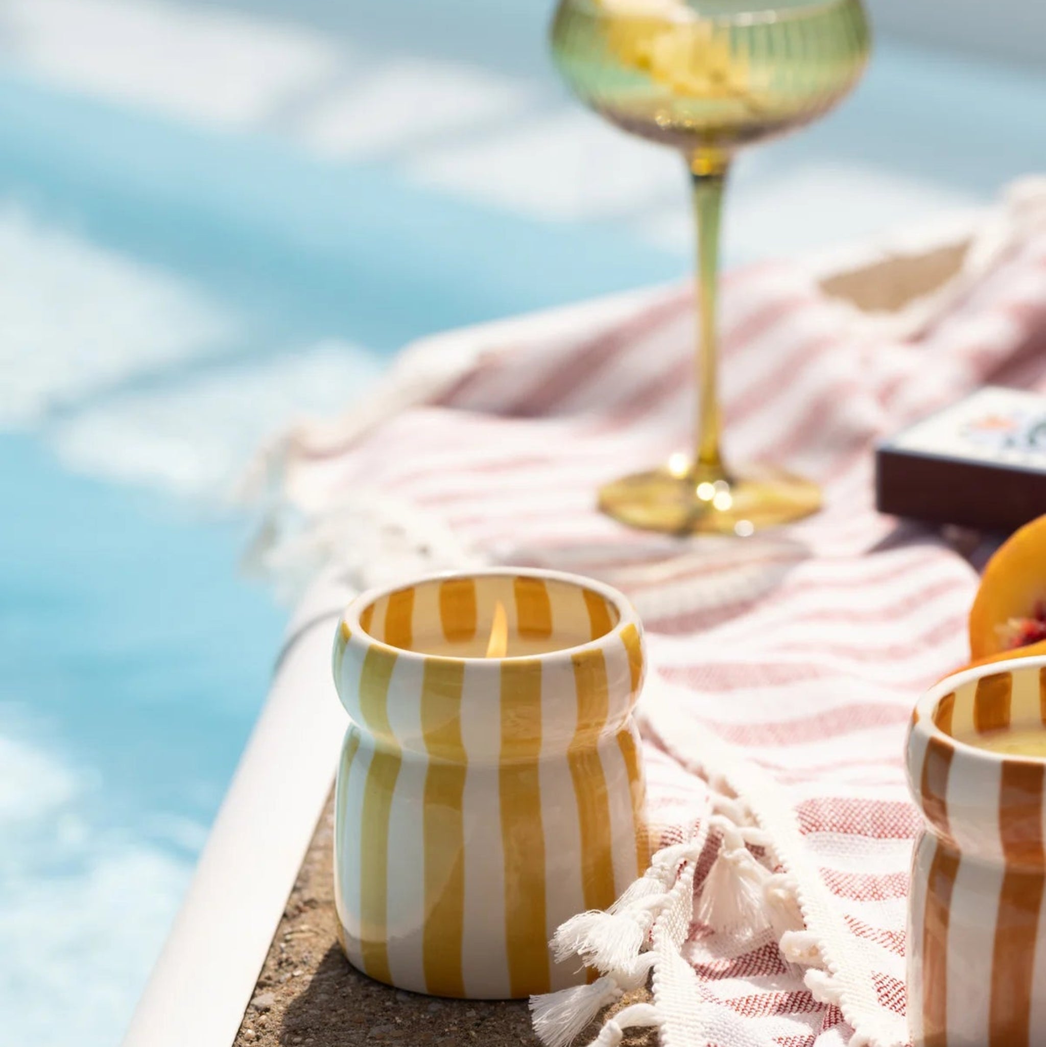 Yellow striped candle and glass with fruit on a towel by a pool