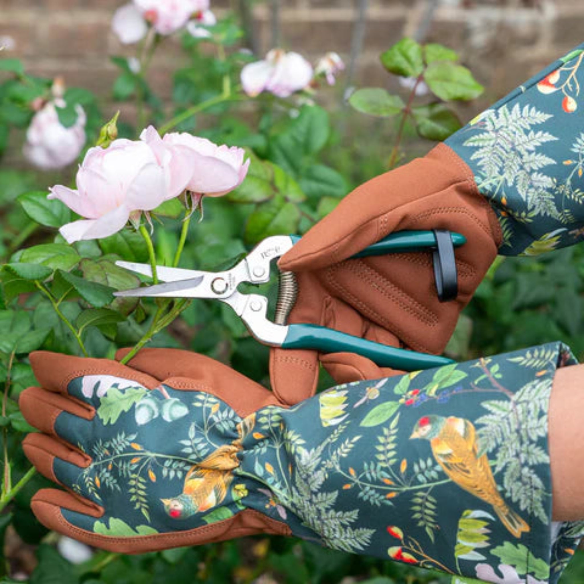 Person wearing gardening gloves holding a pair of shears with flowers in the background