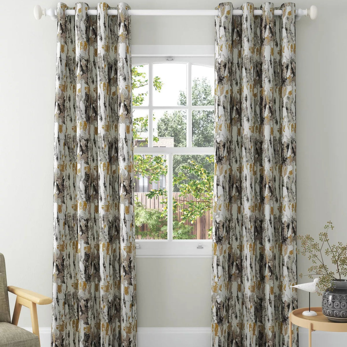 A pair of floor-length taupe grommet curtains hanging on a white rod in a bright, modern room with a window, light wood floor, and a small side table.