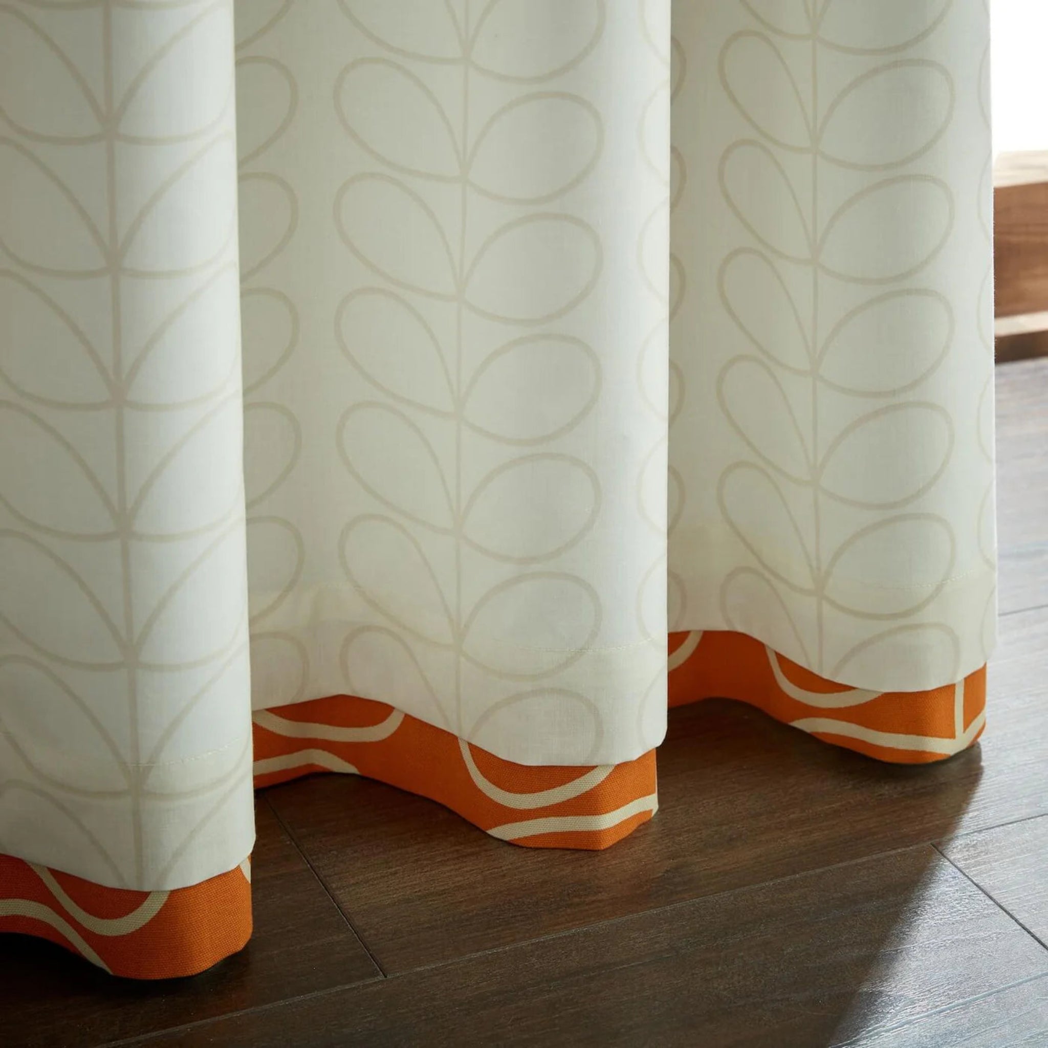 Curtains with a leaf pattern and orange banding on a wooden floor.