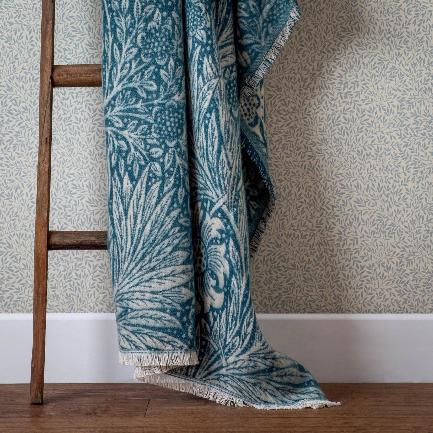 Blue and white patterned throw blanket draped over a wooden ladder against a wallpapered wall.