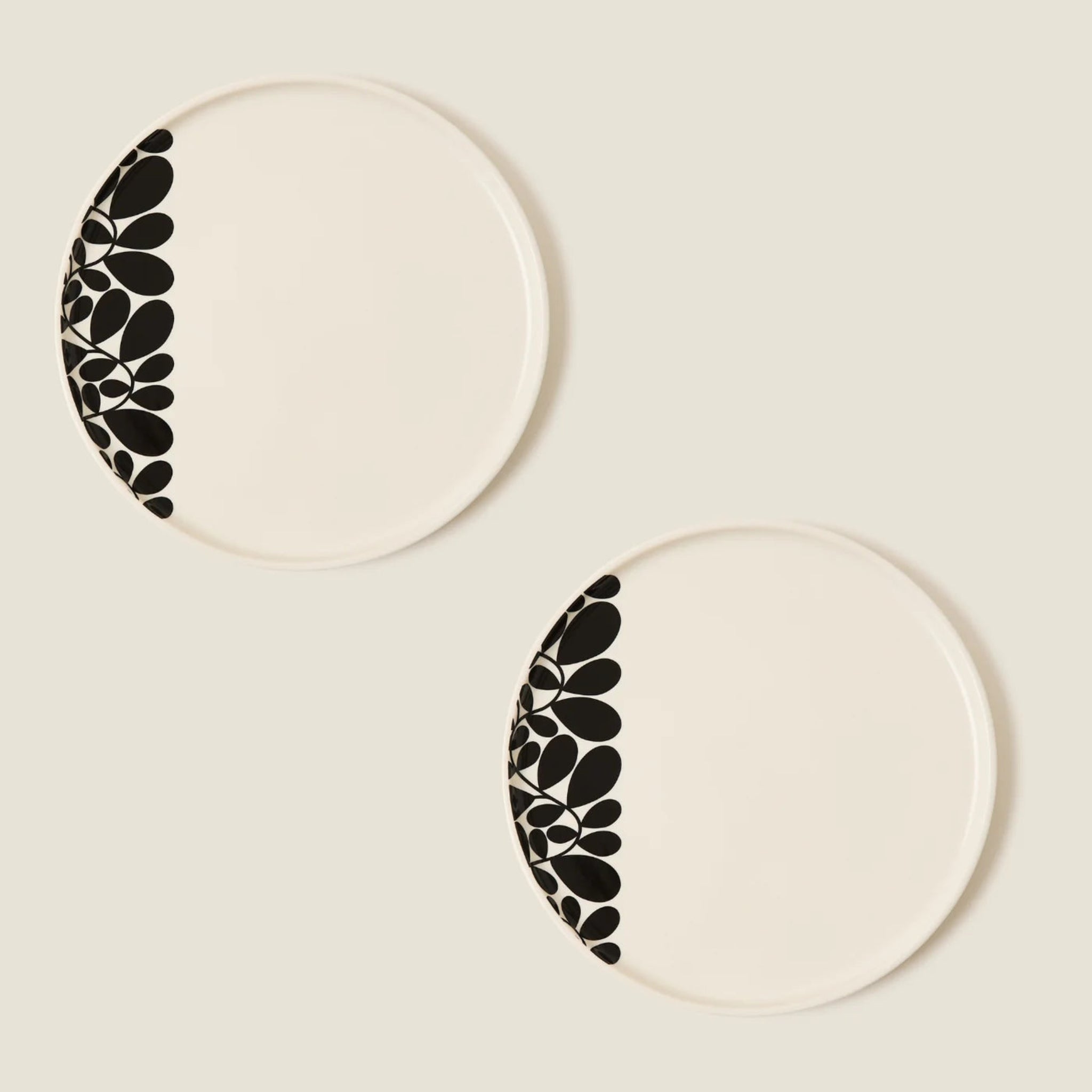Two ceramic plates with black leaf pattern on a beige background
