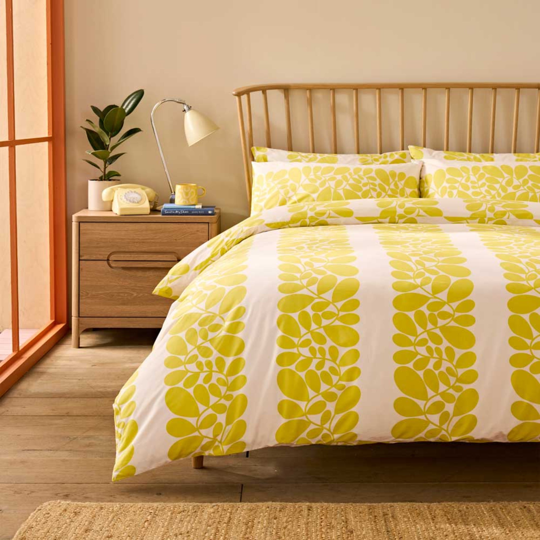 Bedroom with a bed featuring a yellow and white patterned duvet cover, nightstand with lamp and phone.