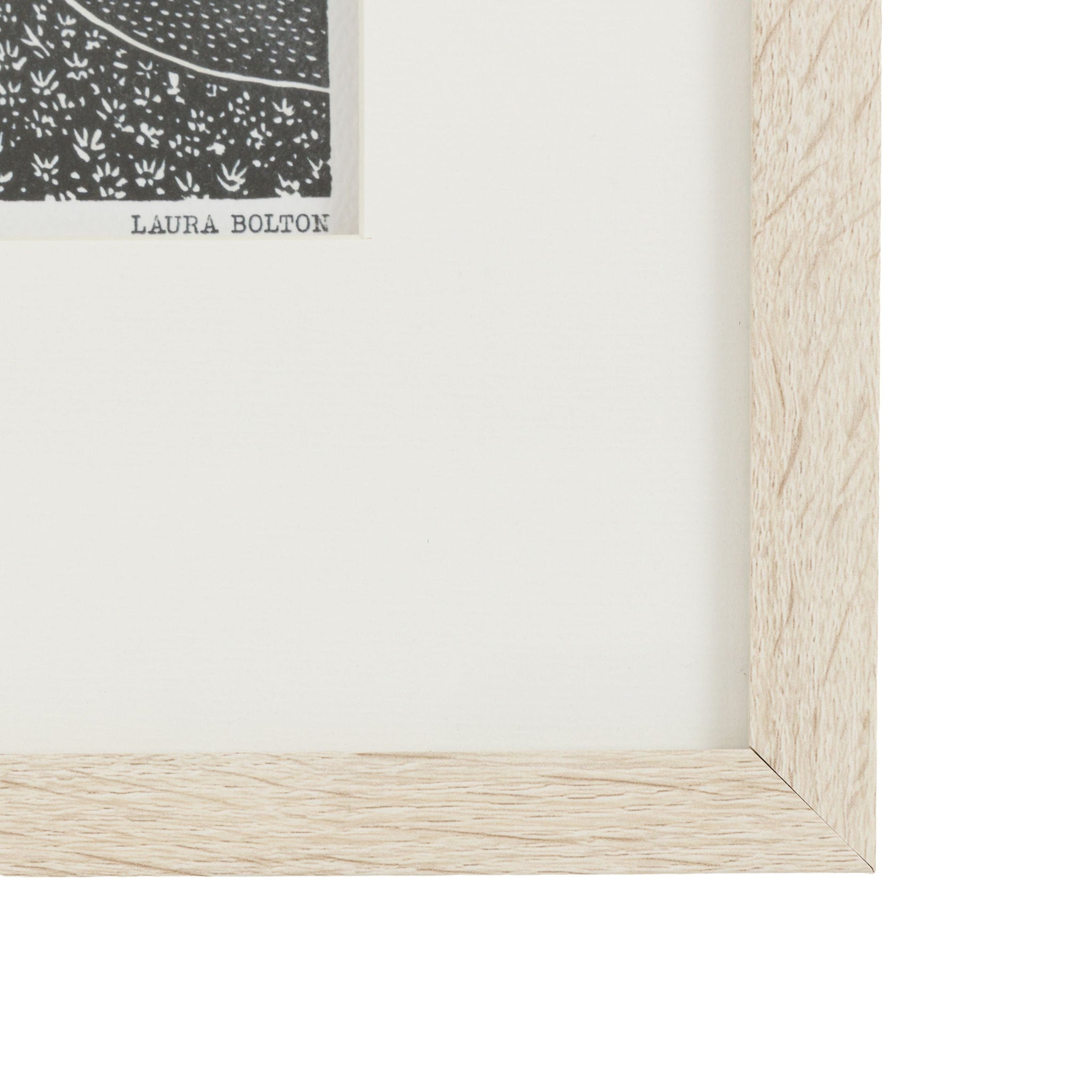 Close-up of a light wood picture frame with a white mat and a small corner of a framed artwork visible.