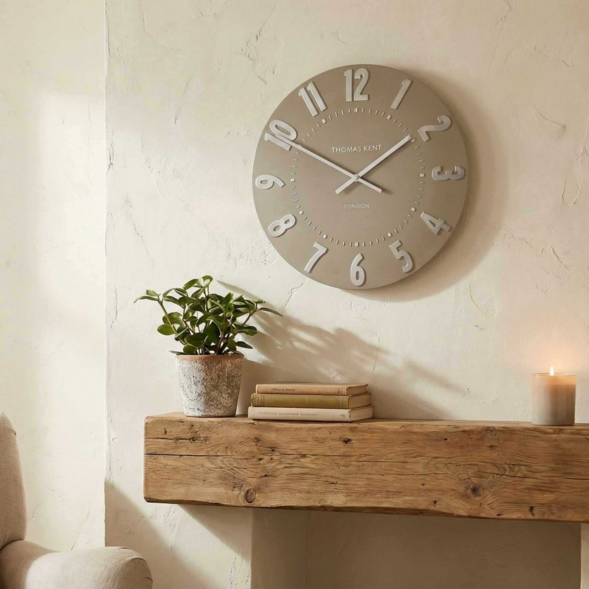 Living room with a clock on the wall, plant, books, and candle on a wooden shelf.