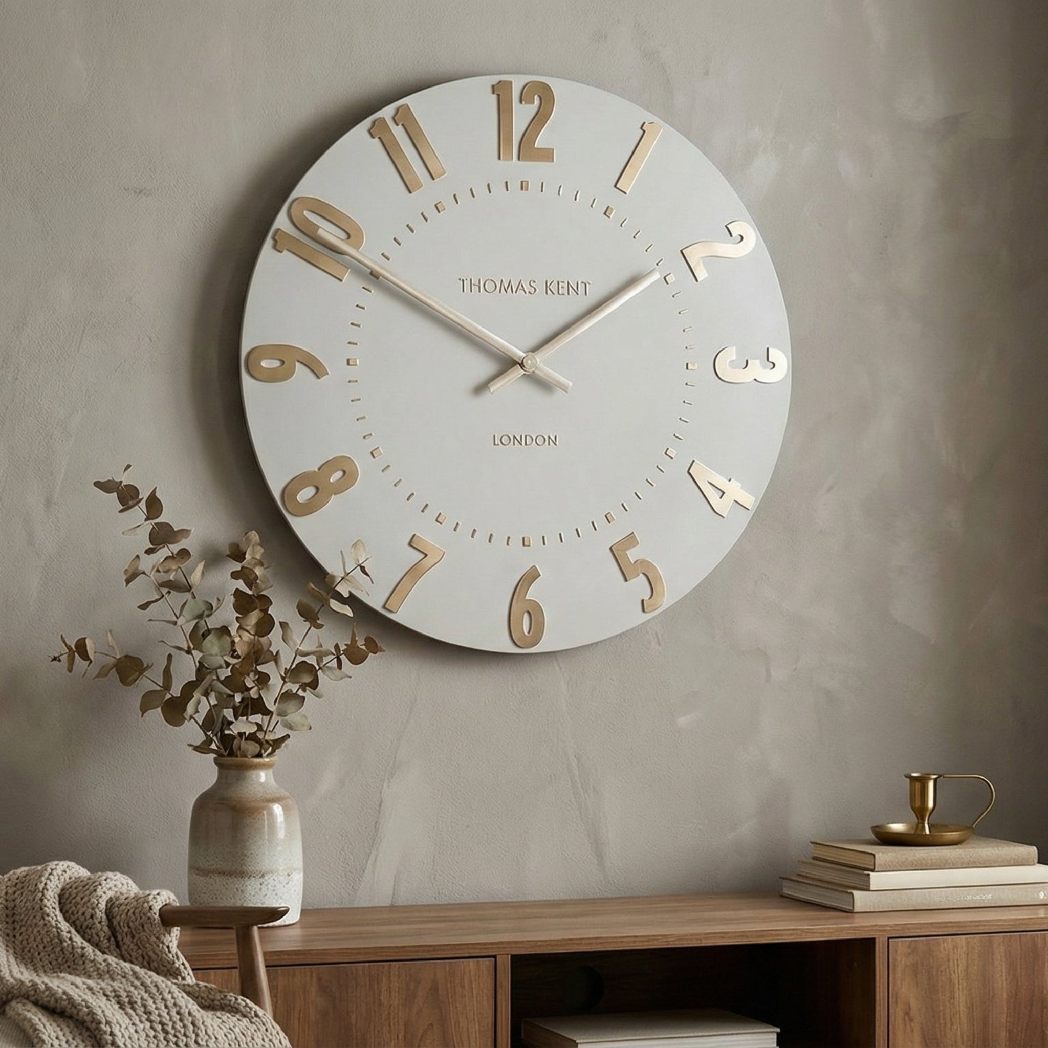 Large wall clock on a gray wall with a wooden side table and chair in a room.