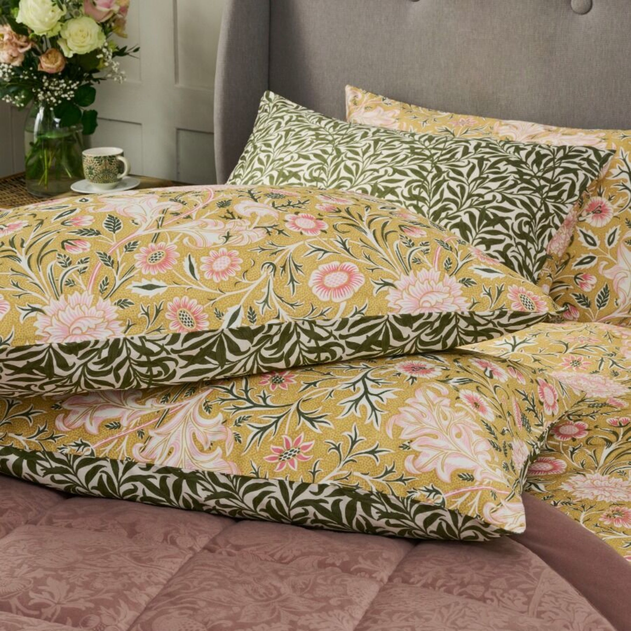 Floral patterned bedding set on a bed with a vase of flowers in the background.