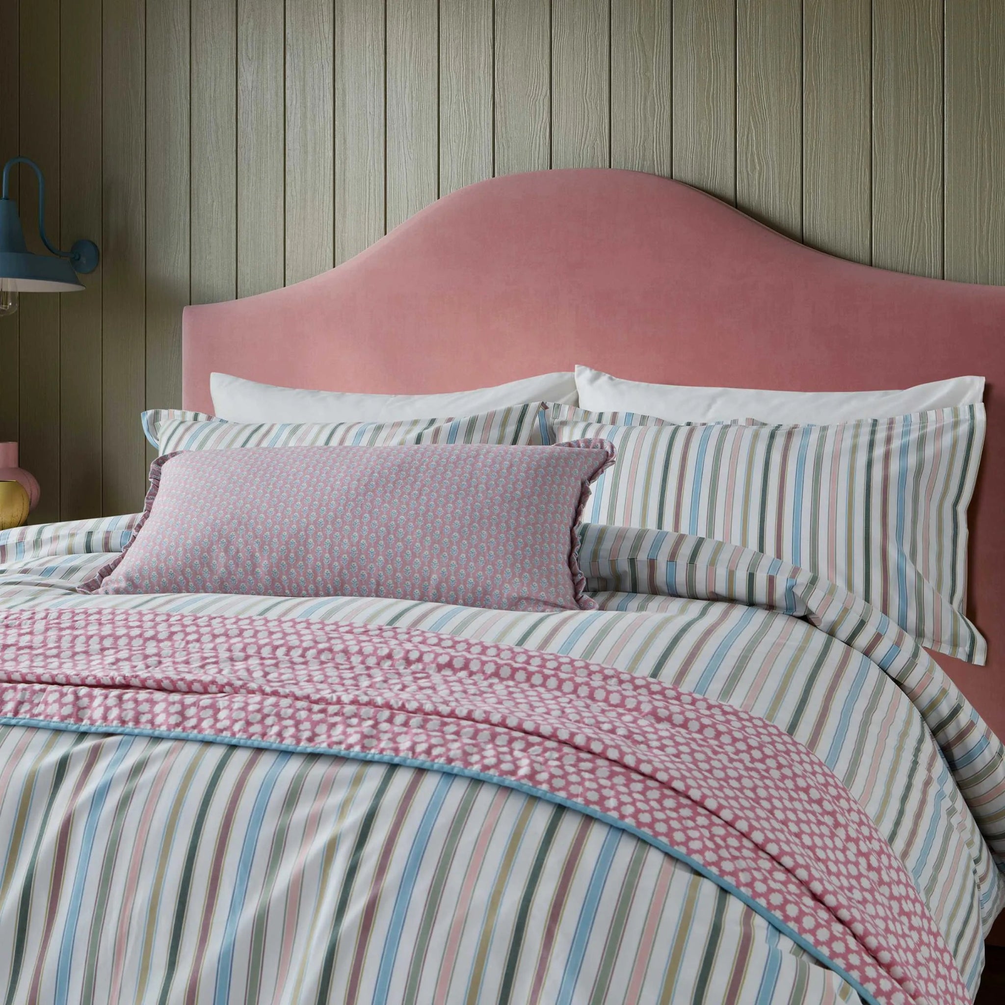 Striped bedding with a pink headboard against a wooden wall.