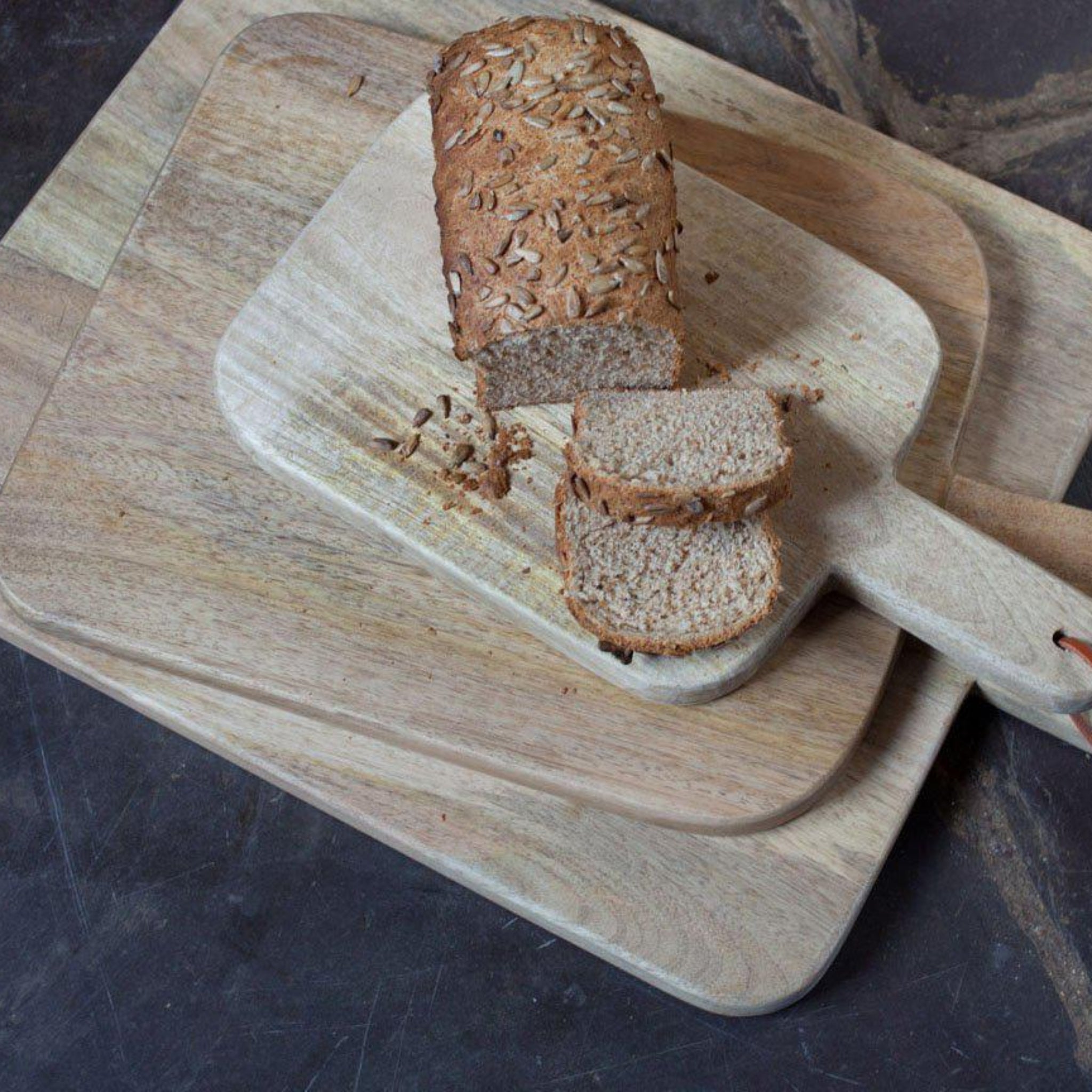 Loaf of bread with slices on a wooden cutting board with a knife on a dark surface