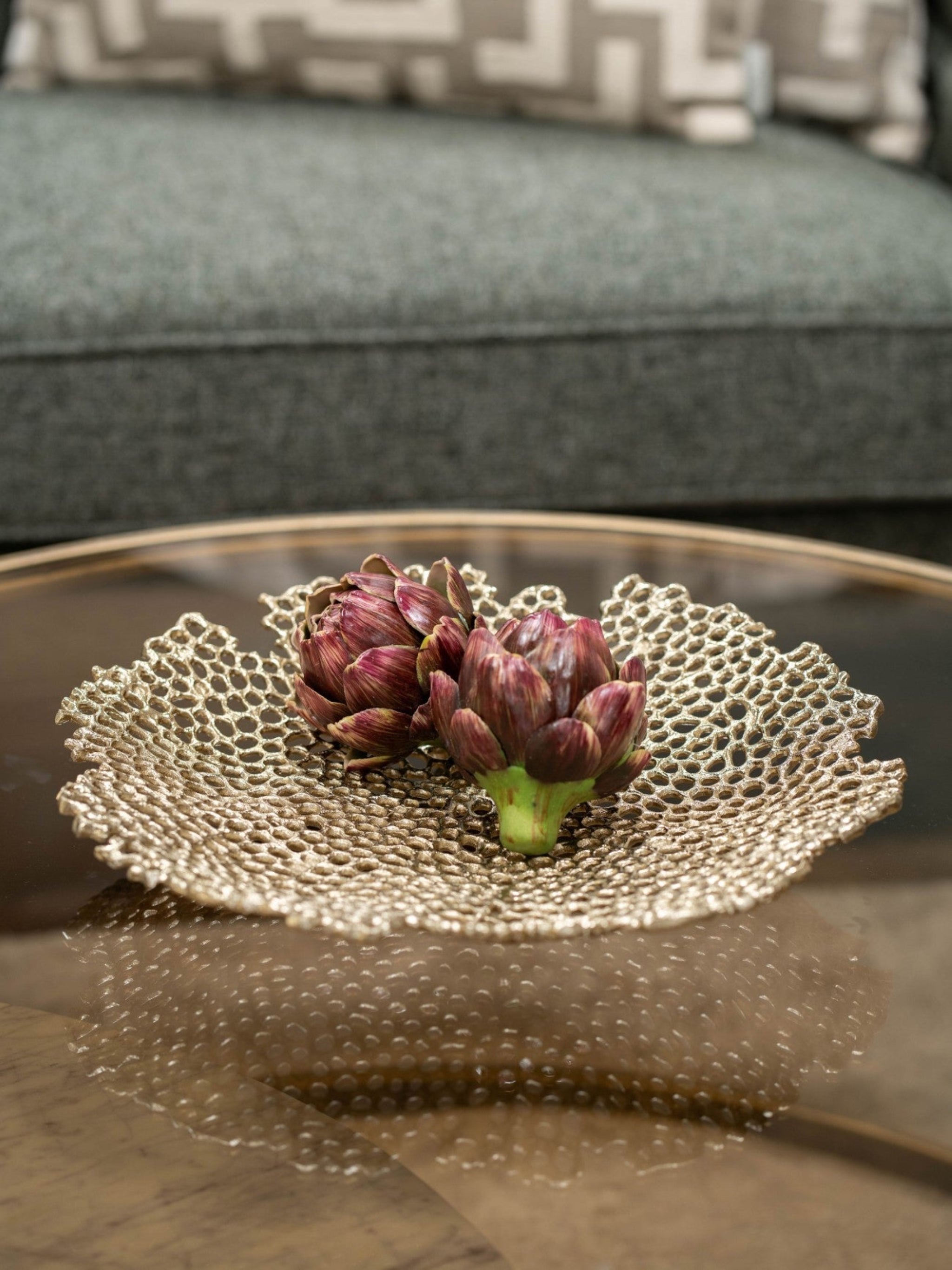 Decorative gold dish with artichokes on a reflective surface