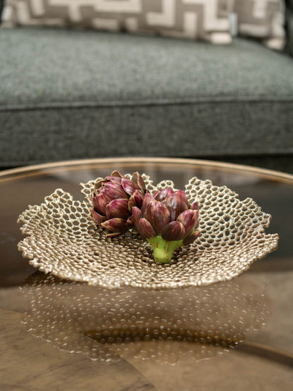 Decorative gold dish with artichokes on a reflective surface