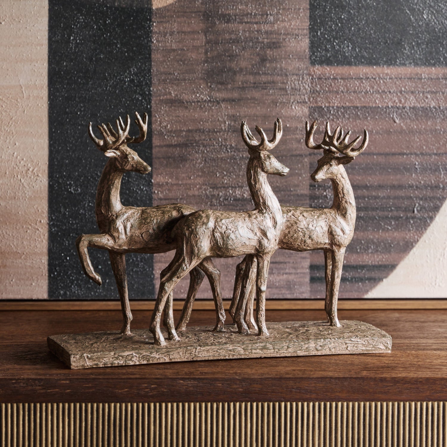 Bronze deer sculpture on a wooden surface with a geometric patterned wall in the background