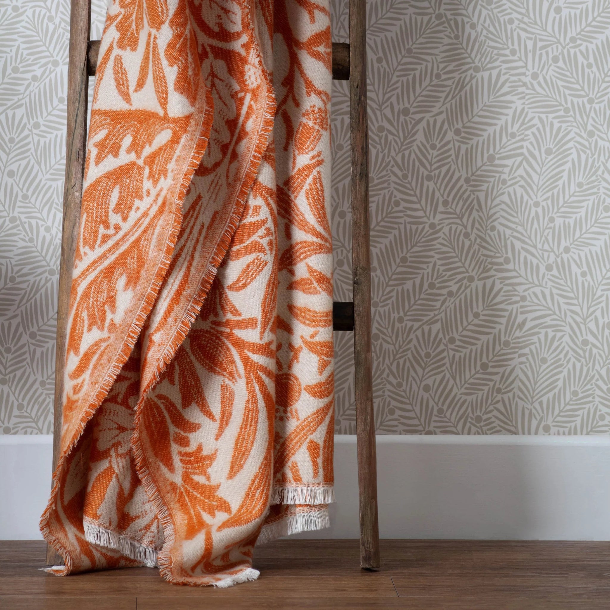 Orange and white patterned blanket draped over a wooden ladder against a neutral background