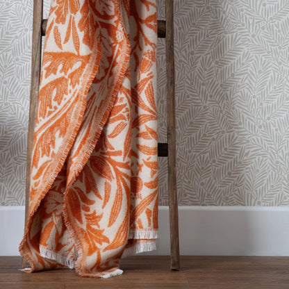 Orange and white patterned blanket draped over a wooden ladder against a neutral background