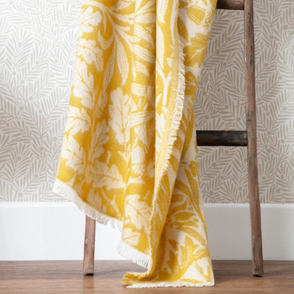 Yellow and white patterned throw blanket draped over a wooden chair against a neutral wall.