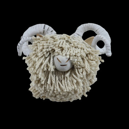 A rustic sheep head wall hanging with shaggy cream wool and white ram horns, mounted on a plain white wall.