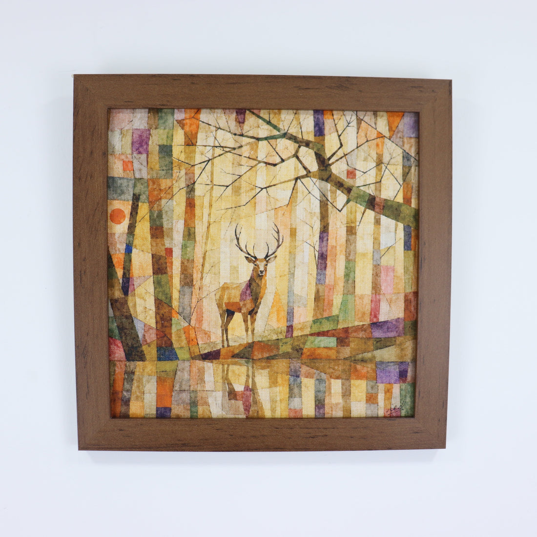 Framed square wall art featuring a deer in a stylized forest scene with vertical tree trunks and branches, shown against a plain white wall.