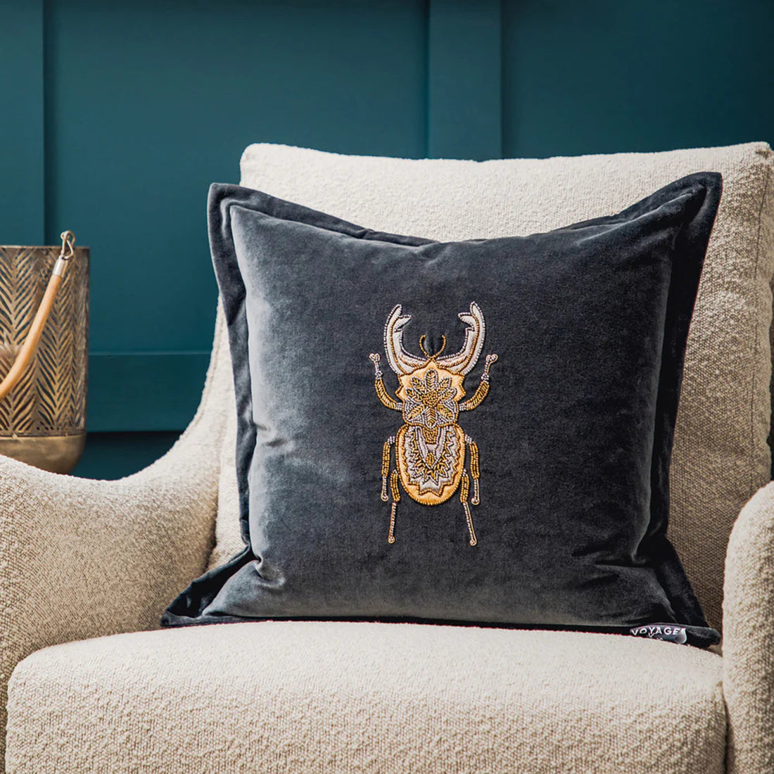 Decorative cushion with embroidered beetle design on a beige armchair against a blue wall.