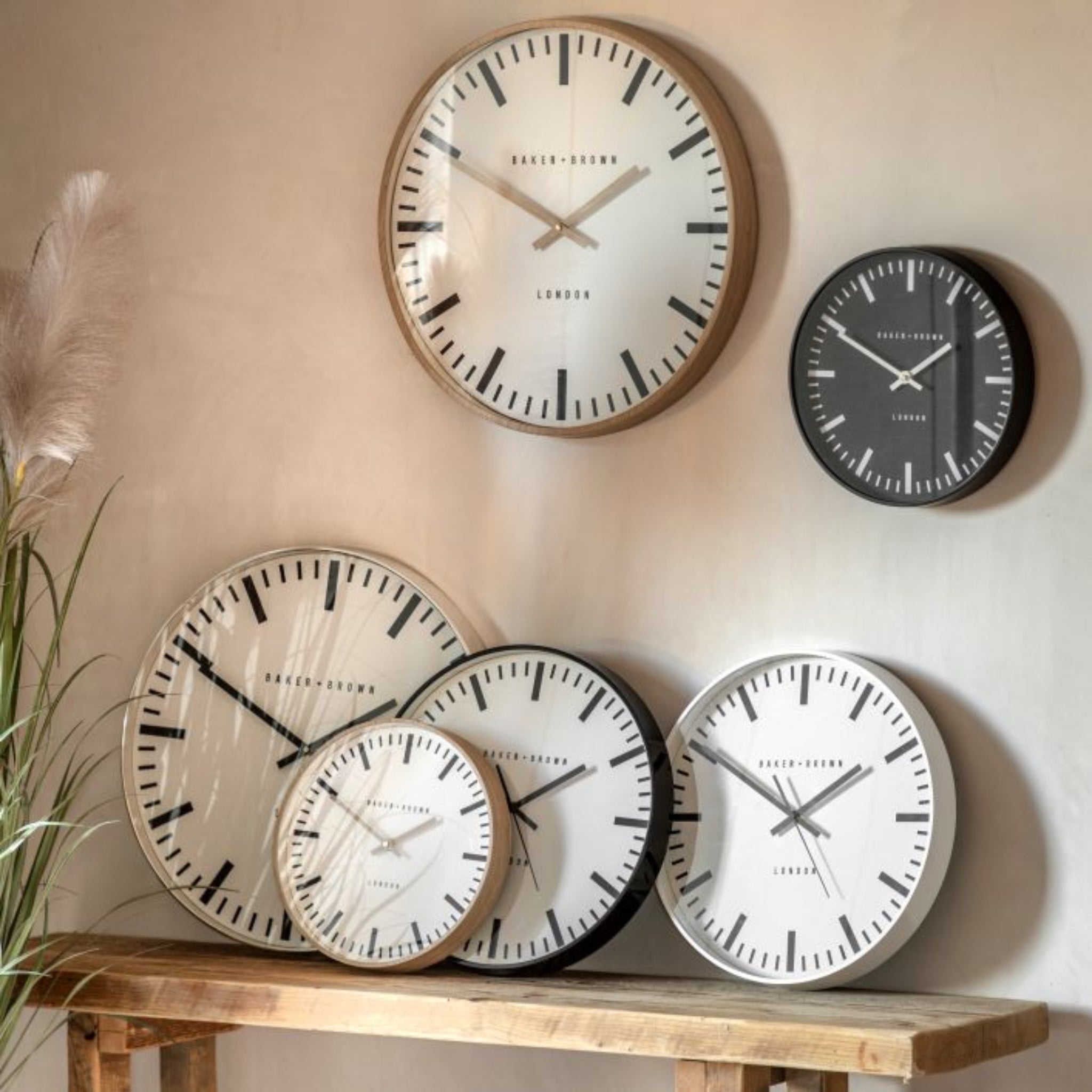 Set of wall clocks on a wooden shelf against a beige wall