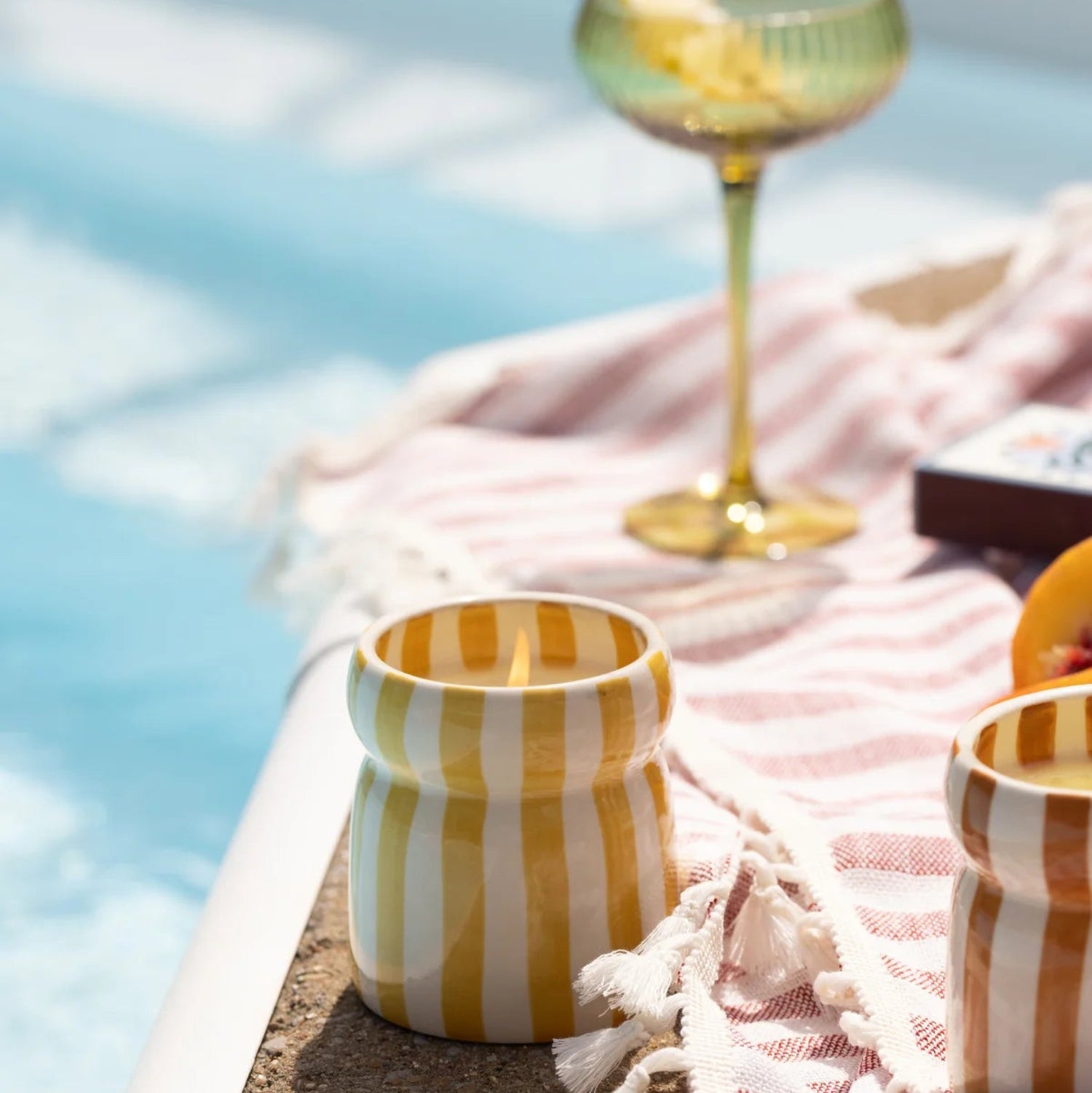 Yellow striped candle and glass with fruit on a towel by a pool