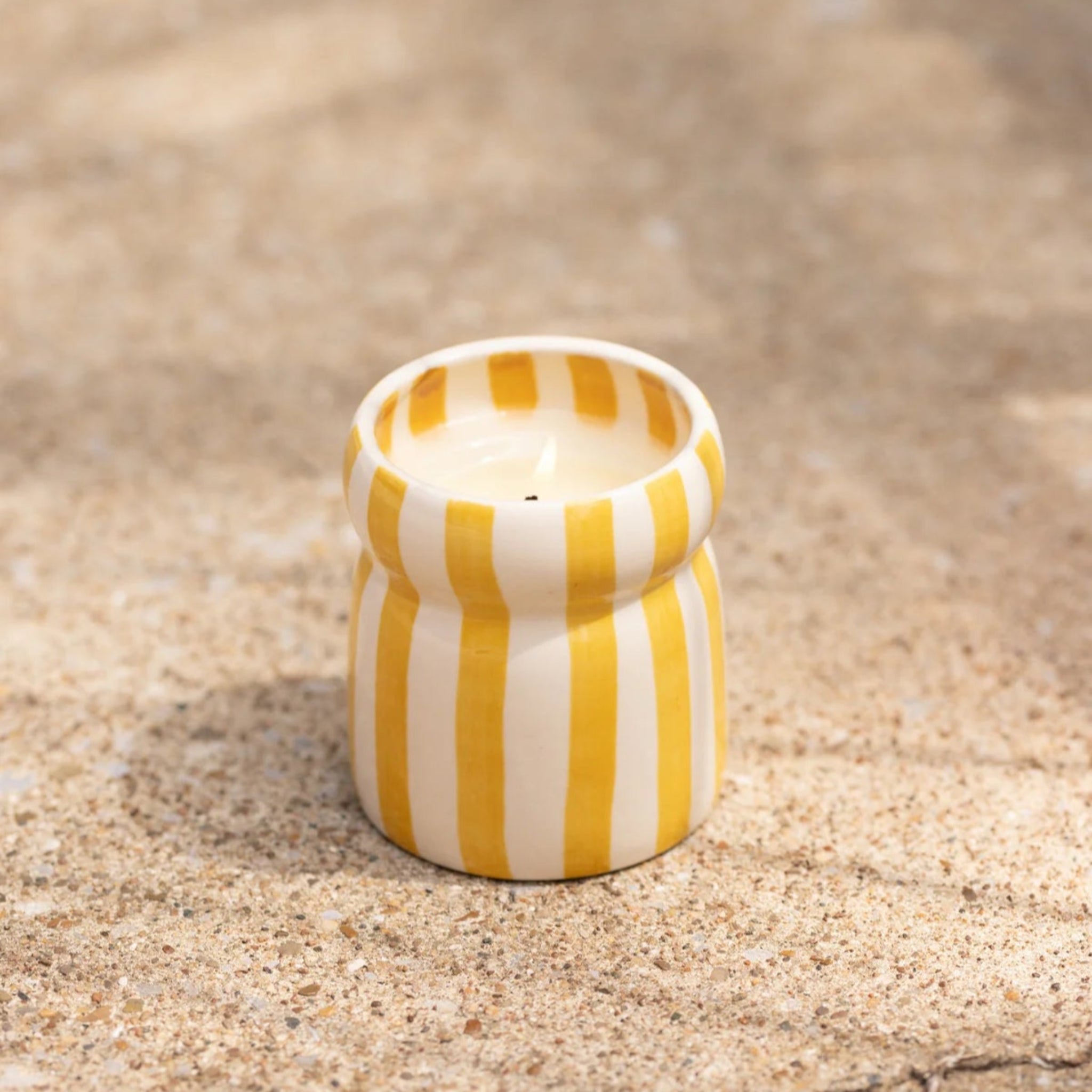 Yellow and white striped ceramic container on sandy ground