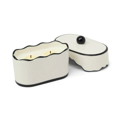 White ceramic container with black rim holding a lit candle on a white background