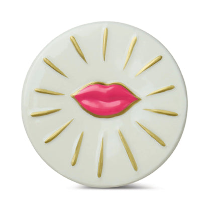 Round white object with pink lips and gold accents on a white background