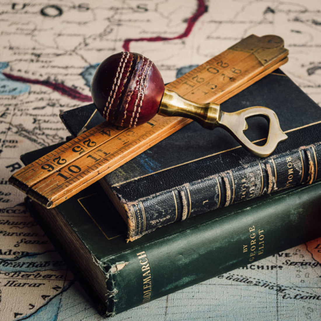 Cricket ball, bottle opener, and wooden ruler on vintage books with a map background