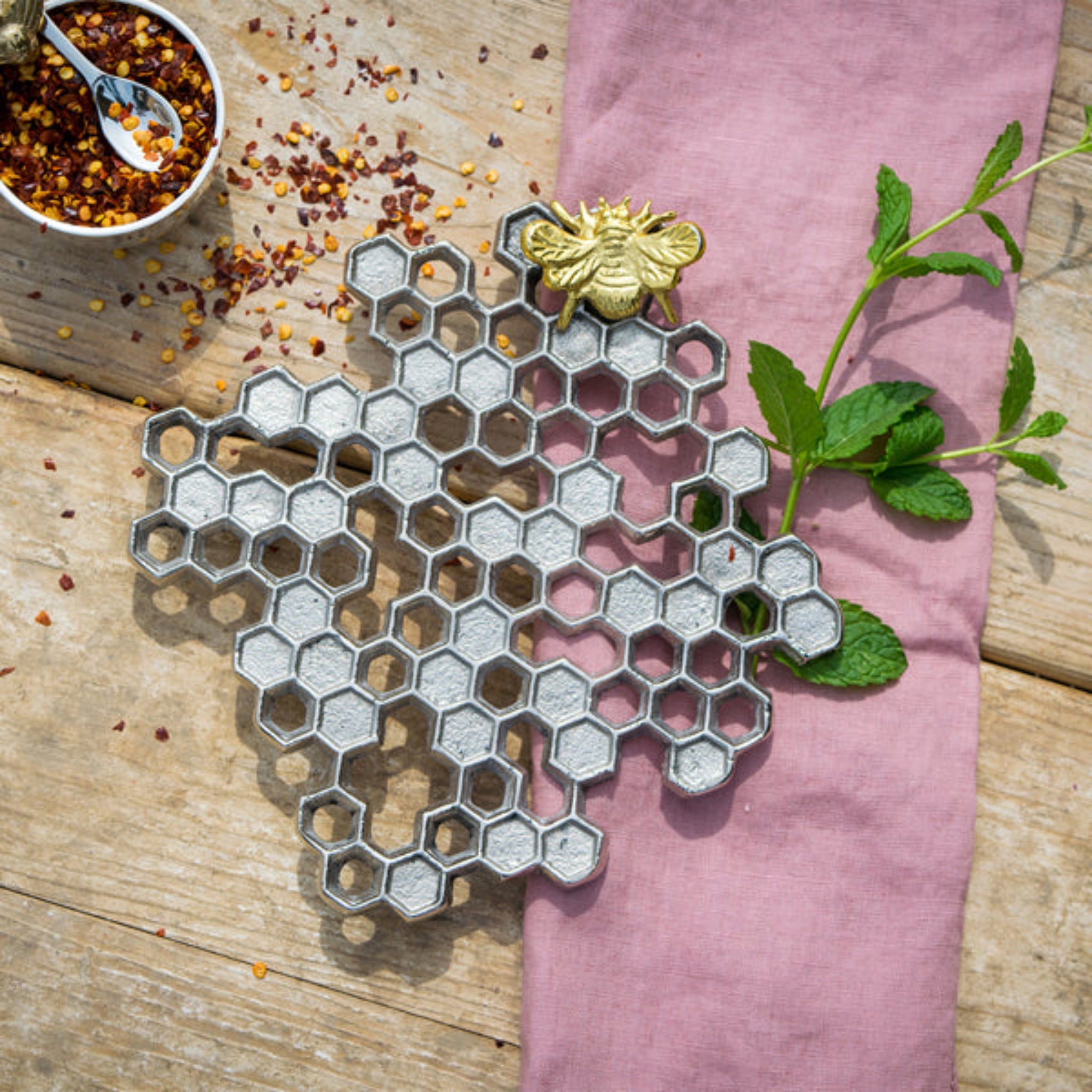 Metal honeycomb decorative item with a bee on a pink cloth and wooden surface.