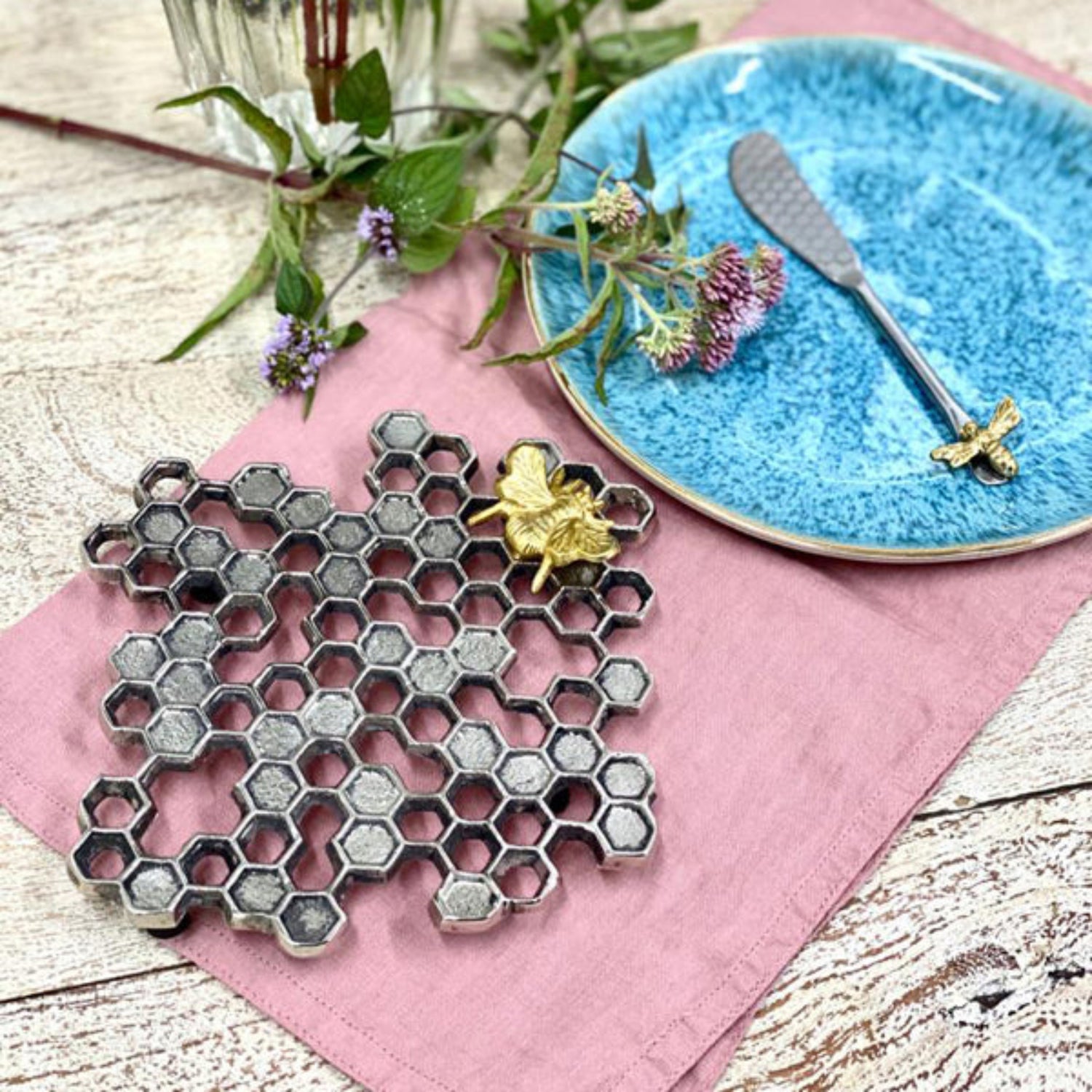 Honeycomb-shaped trivet with bee design on a pink cloth with a blue plate in the background.