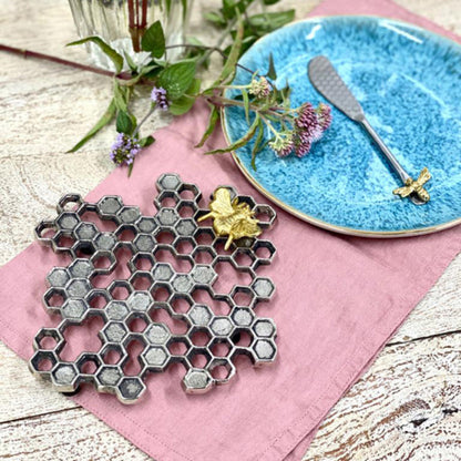 Honeycomb-shaped trivet with bee design on a pink cloth with a blue plate in the background.