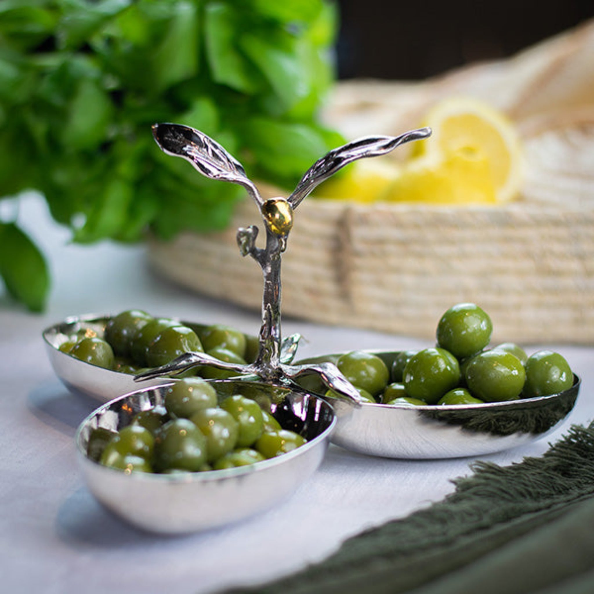 Silver olive dish with green olives on a light surface, blurred background