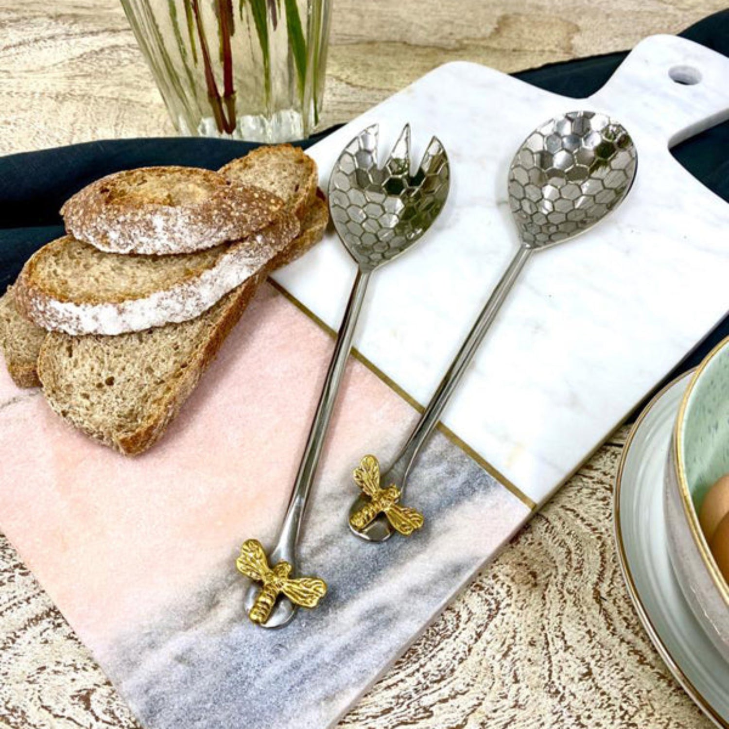 Two decorative spoons with honeycomb design on a marble surface with bread and a glass.