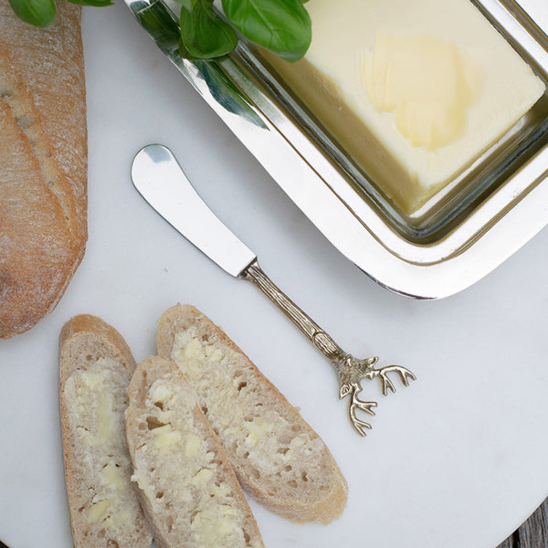 Butter dish with a knife featuring a deer design, bread slices with butter, and a loaf of bread on a white surface.