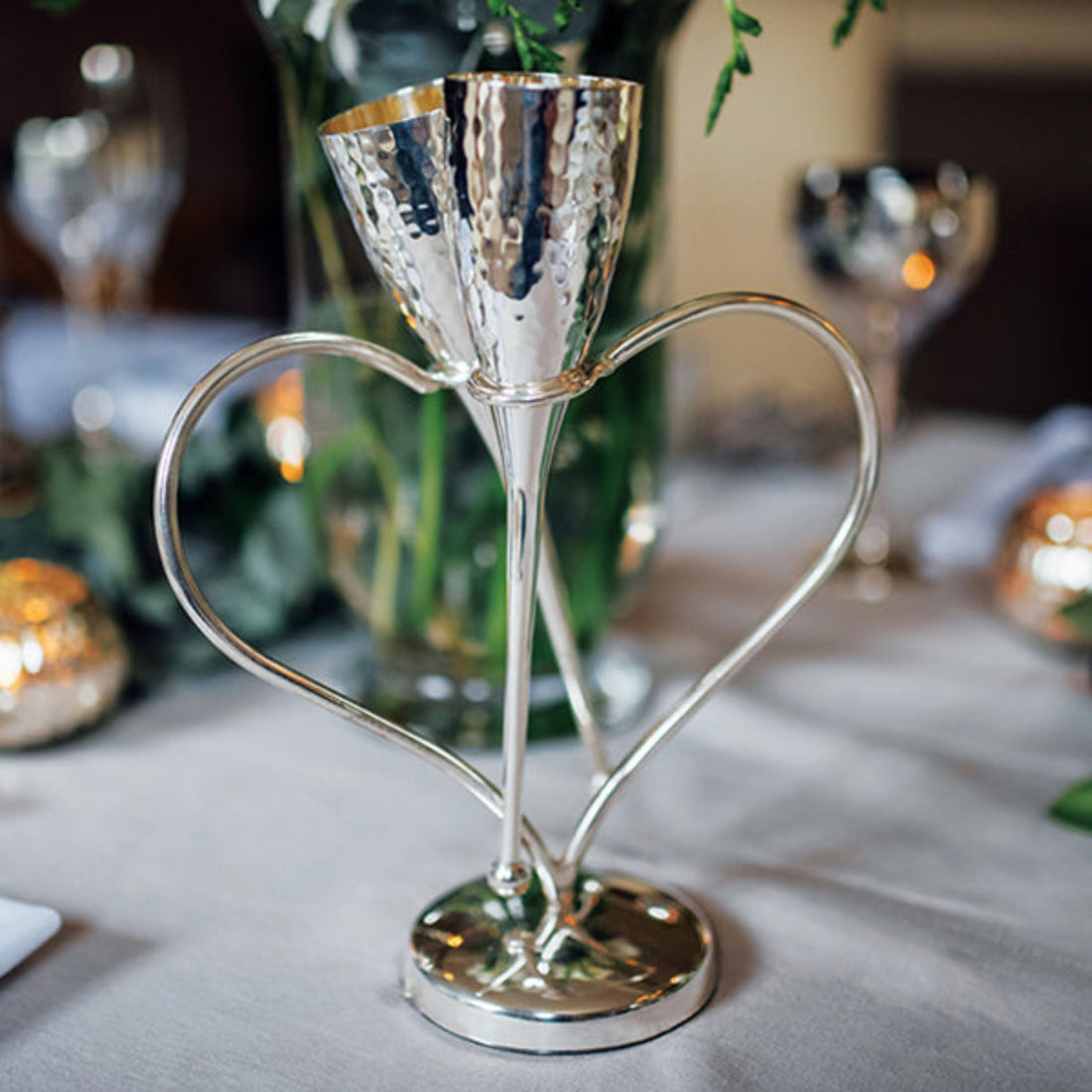 Silver candle holder with heart-shaped base on a table with blurred background