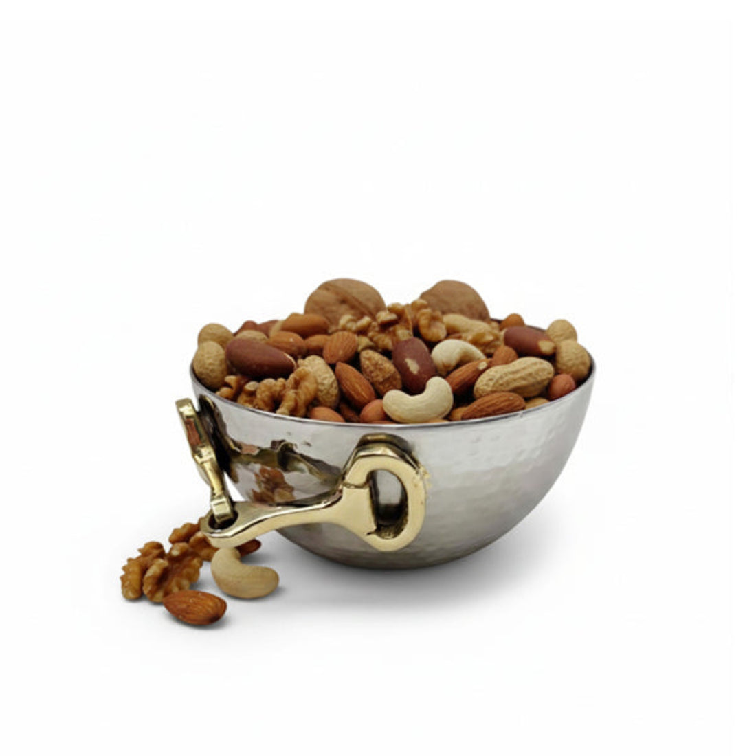 A hammered silver metal bowl filled with mixed nuts and seeds, featuring a decorative gold-toned handle and spout, with a few nuts spilled onto the white surface. The bowl is photographed on a clean white background.