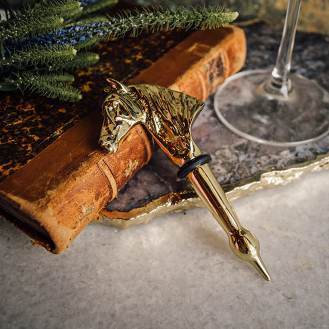 Gold wine bottle stopper on a stone surface with a book and greenery in the background