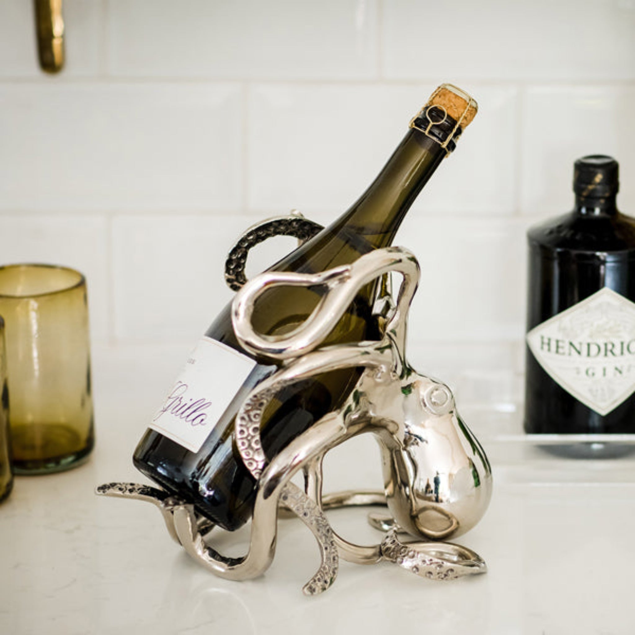 Silver wine bottle holder with a bottle of wine on a kitchen counter.