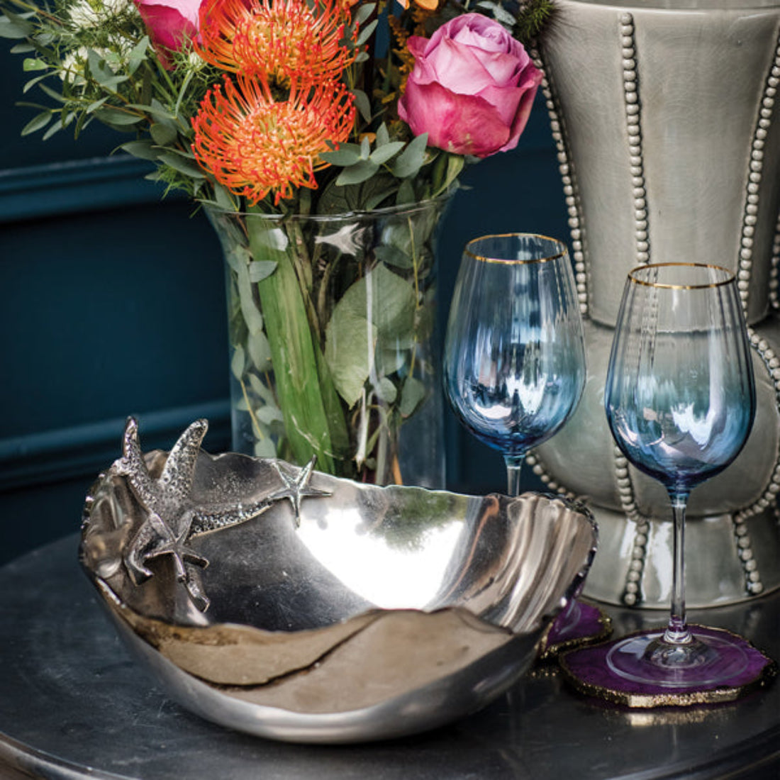 Decorative bowl with starfish design, vase of flowers, and two blue wine glasses on a table.
