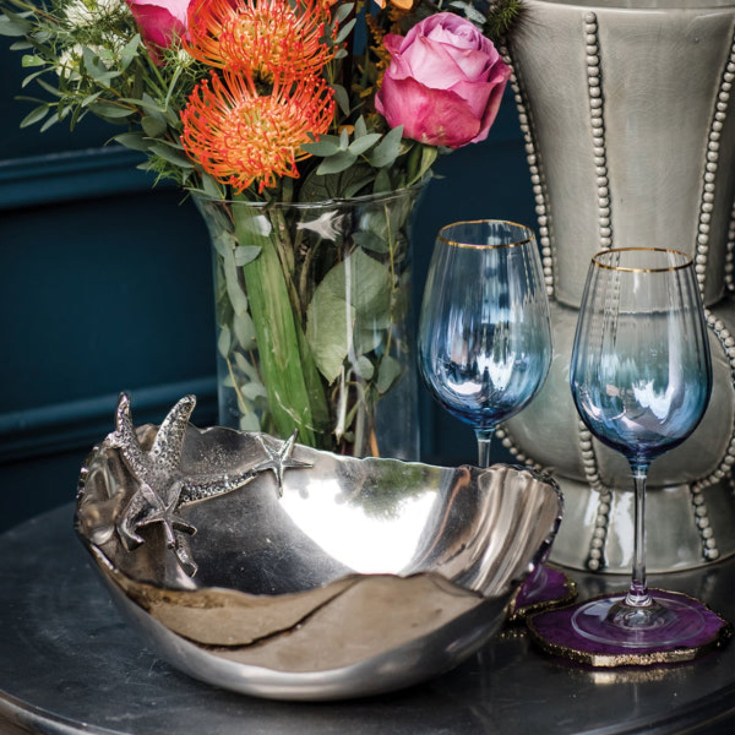 Decorative bowl with starfish design, vase of flowers, and two blue wine glasses on a table.