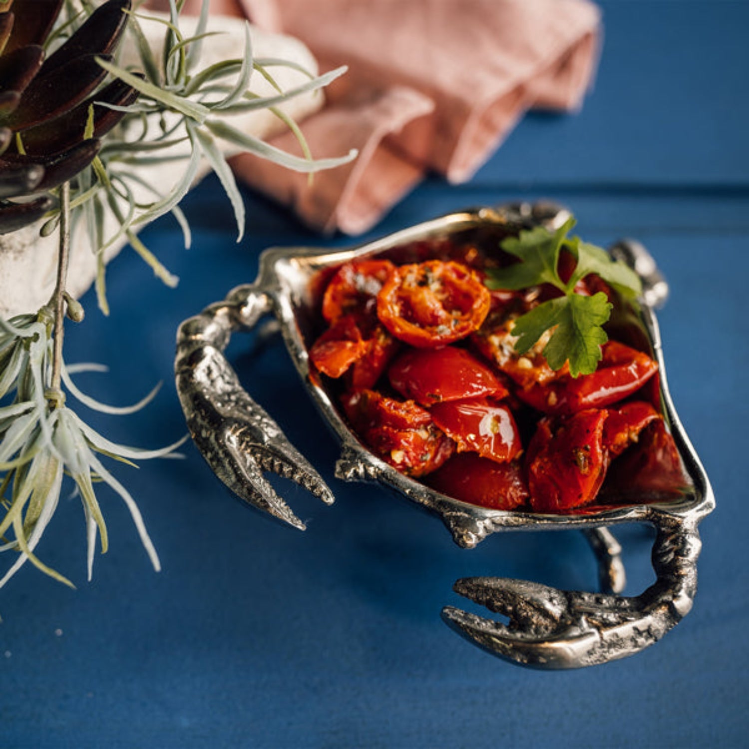 Metallic crab shell container filled with red tomatoes on a blue background