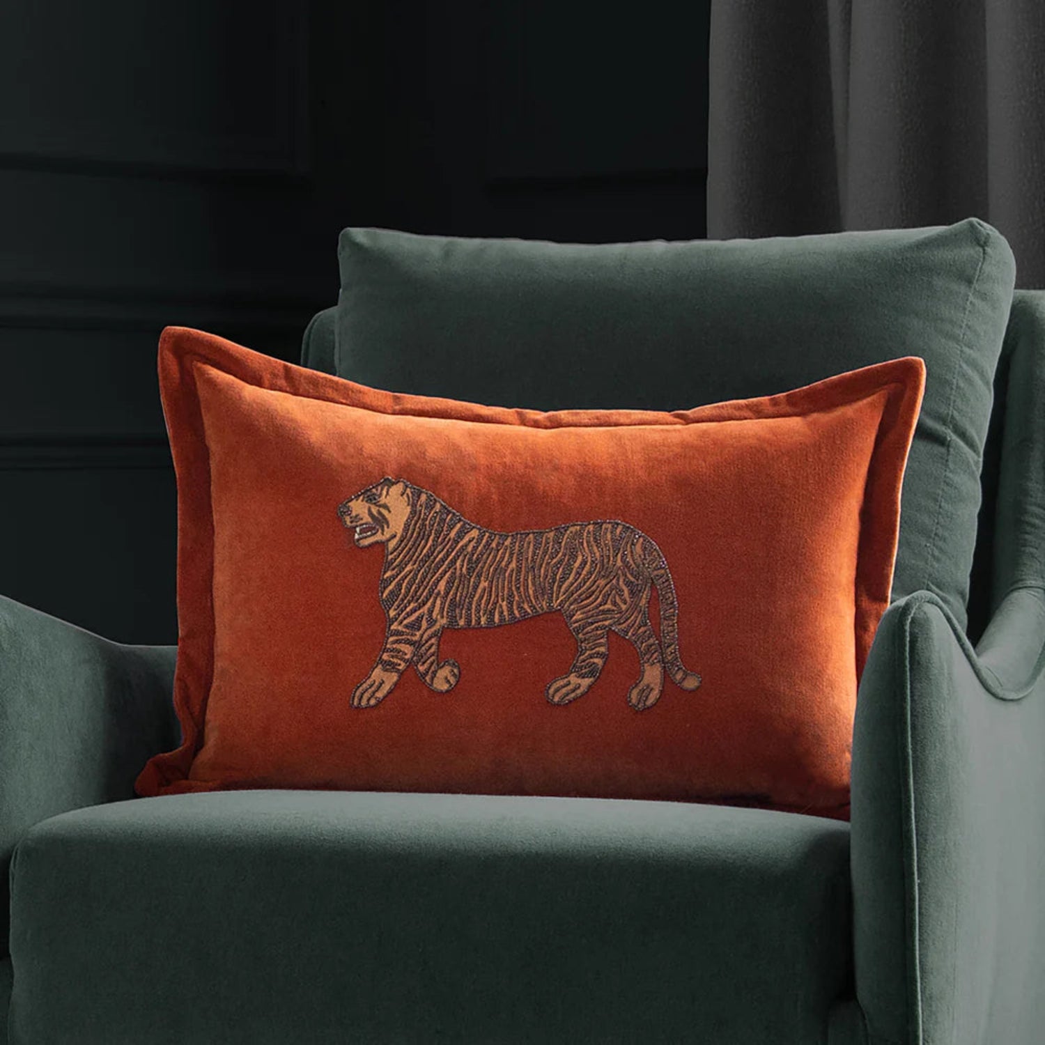 Orange pillow with a tiger design on a green armchair against a dark background