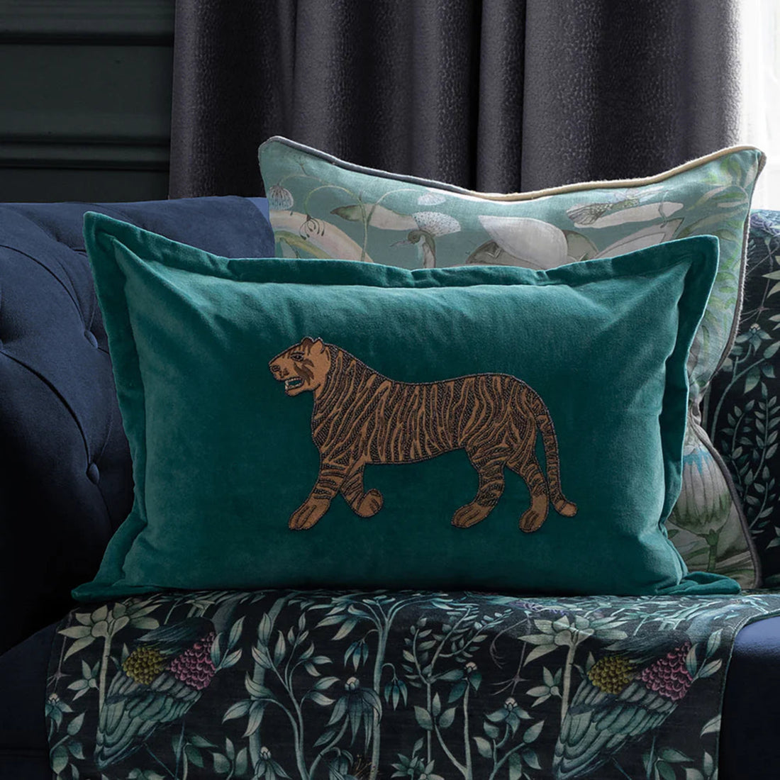 Teal pillow with embroidered tiger design on a patterned sofa
