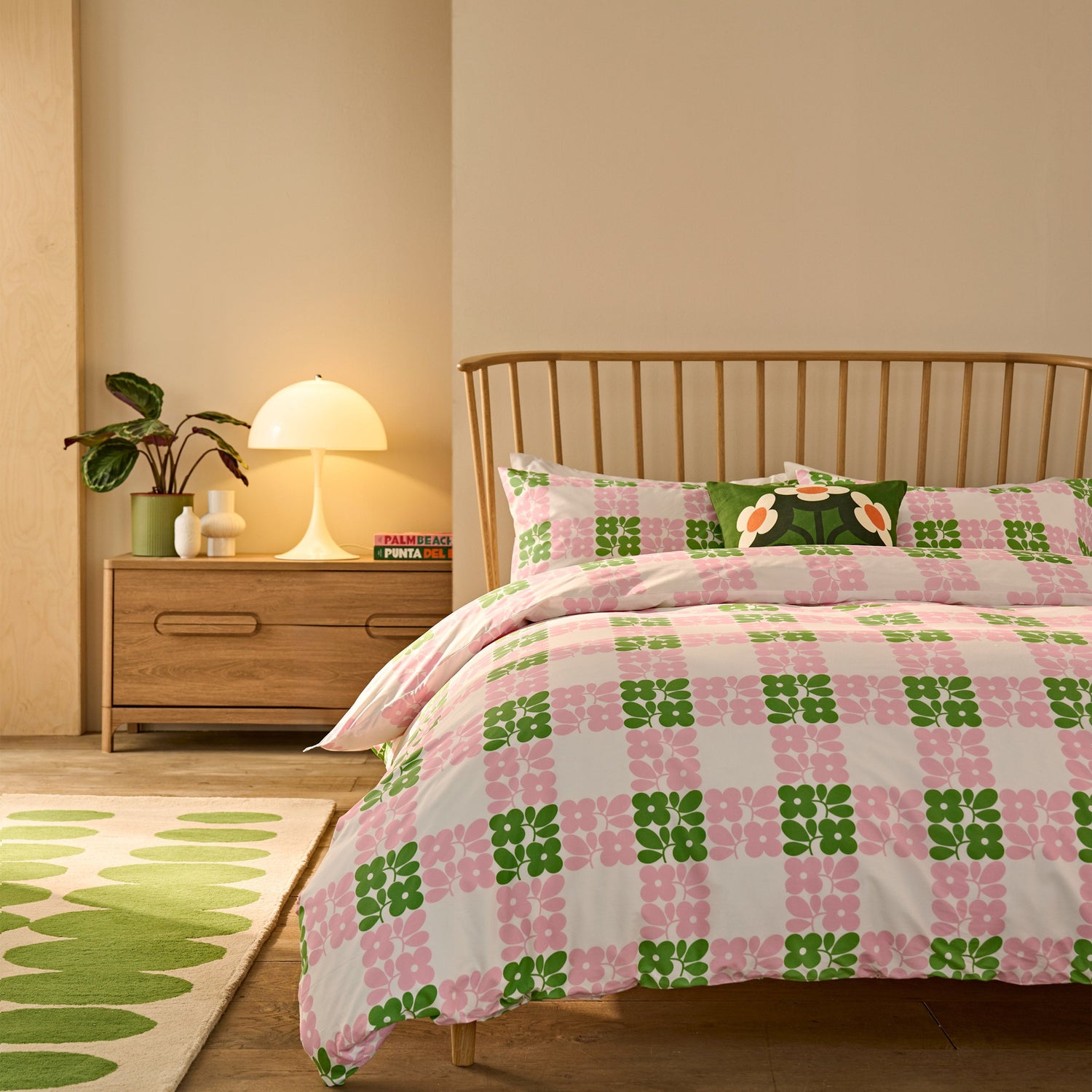Bedroom with a bed featuring a pink and green checkered comforter, wooden nightstand, and lamp.