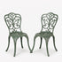 Two green metal chairs with intricate designs on a white background