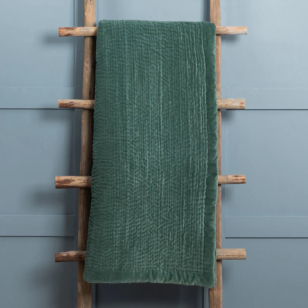 Green textured towel on a wooden ladder against a gray wall