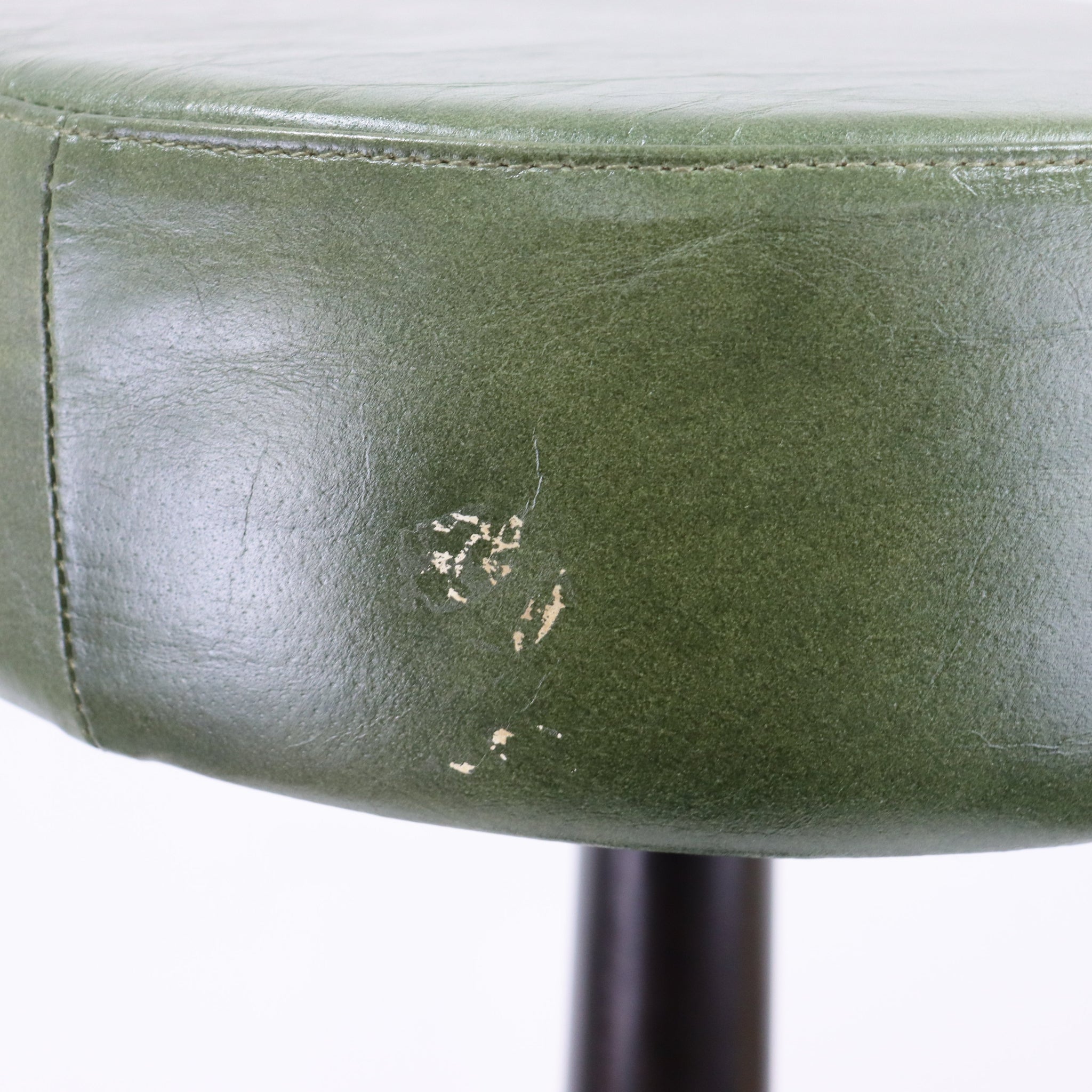 Close-up of a green leather stool with visible wear and tear on a white background