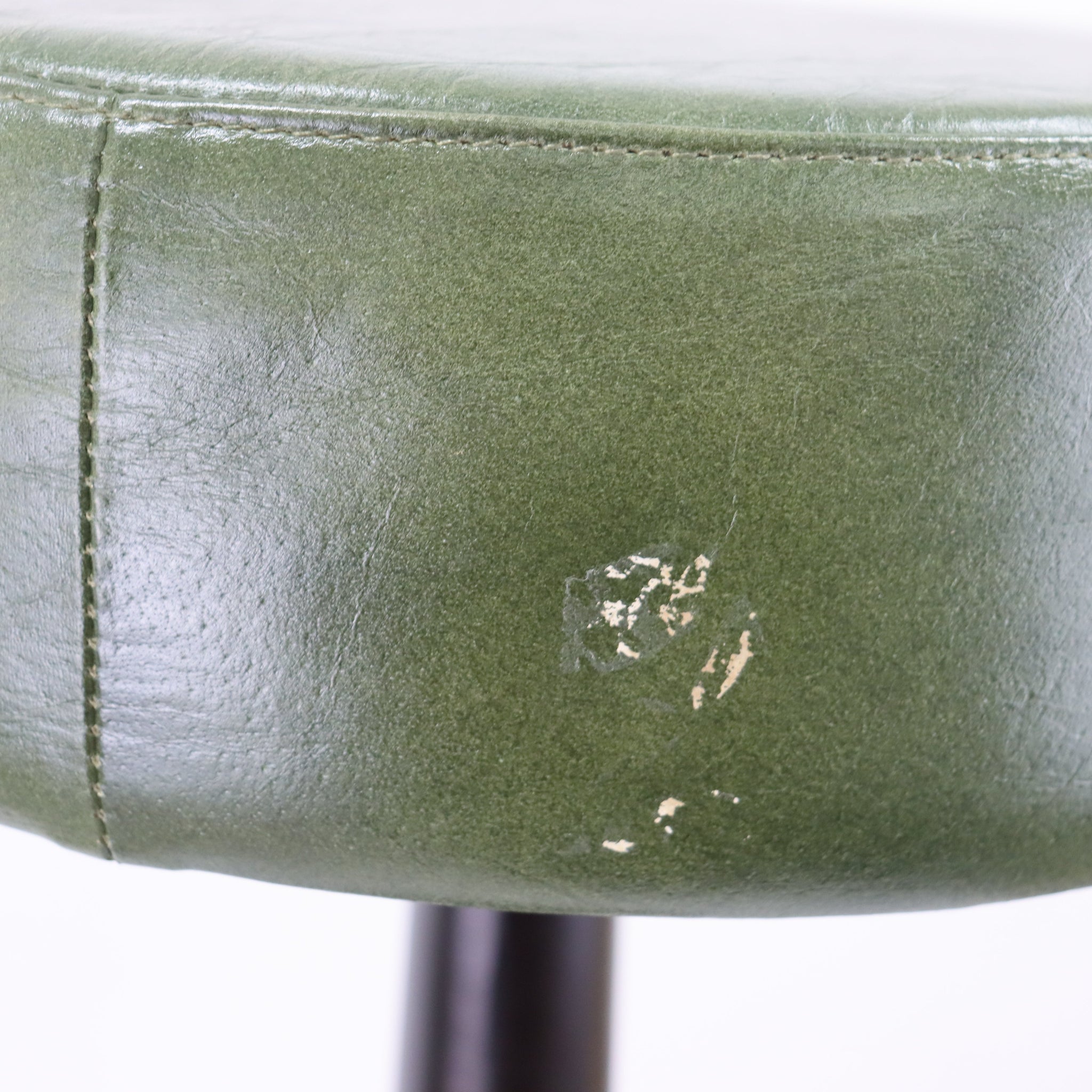 Close-up of a green leather chair with a noticeable scratch on a white background